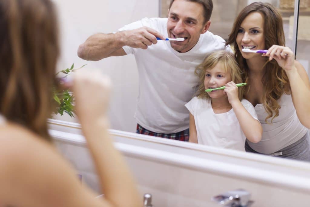 Famiglia che si lava i denti di fronte a uno specchio per combattere sanguinamento gengivale